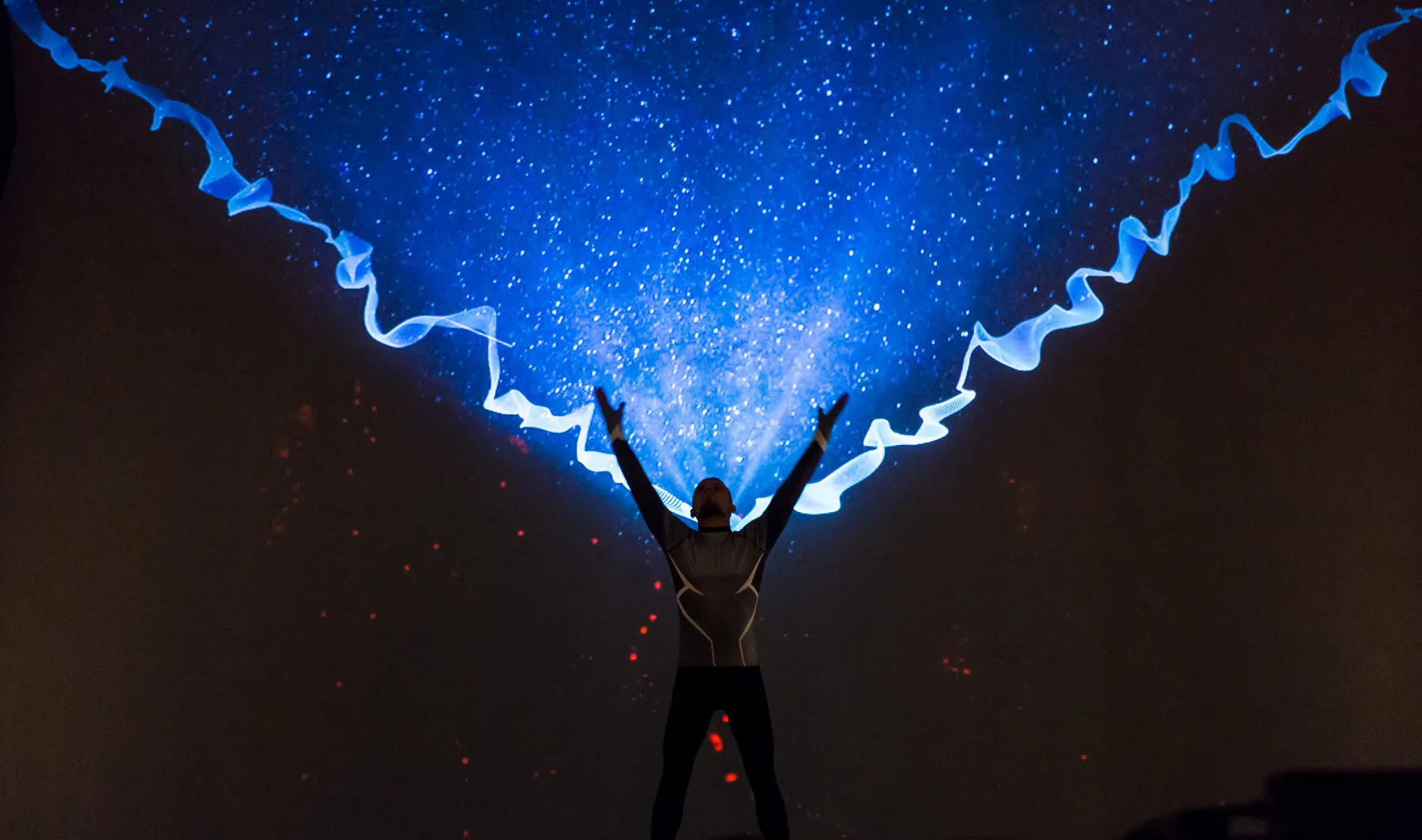A performer with raised arms beneath a vault of blue laser beams