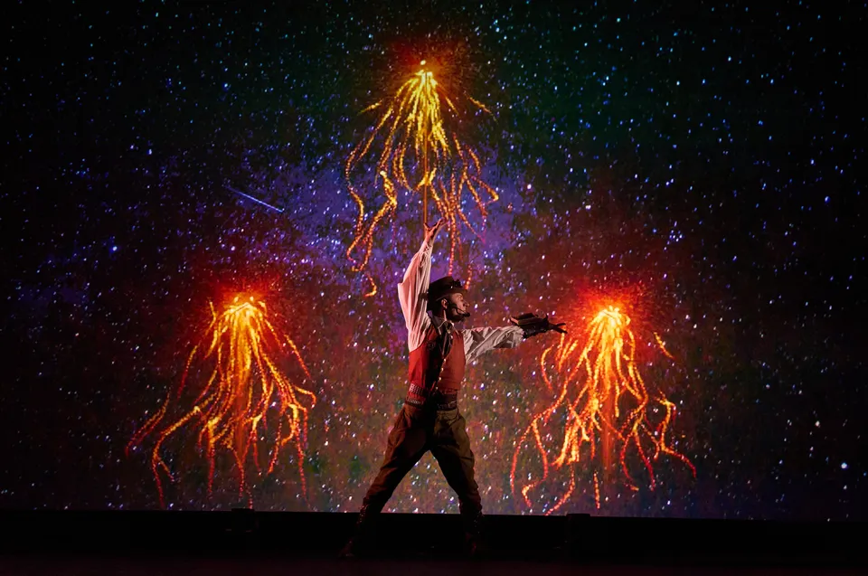 A performer between showers of stage sparks against a starfield backdrop