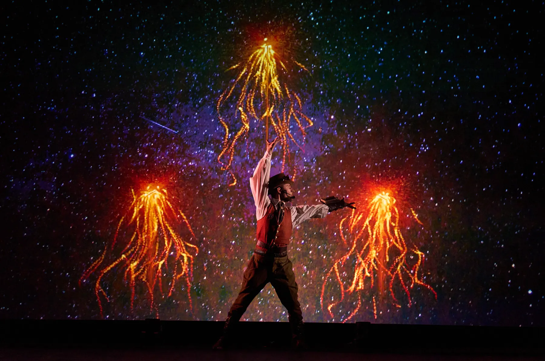 A performer between showers of stage sparks against a starfield backdrop