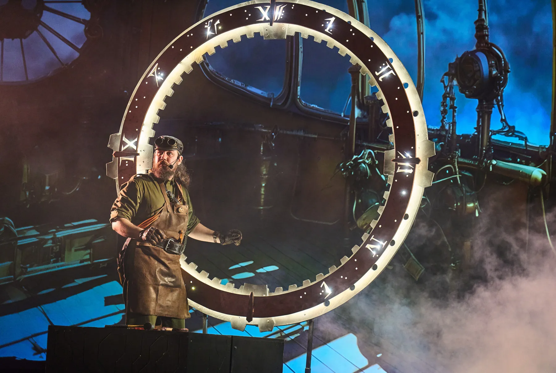 A large time-machine wheel with a dial and a performer in stage smoke