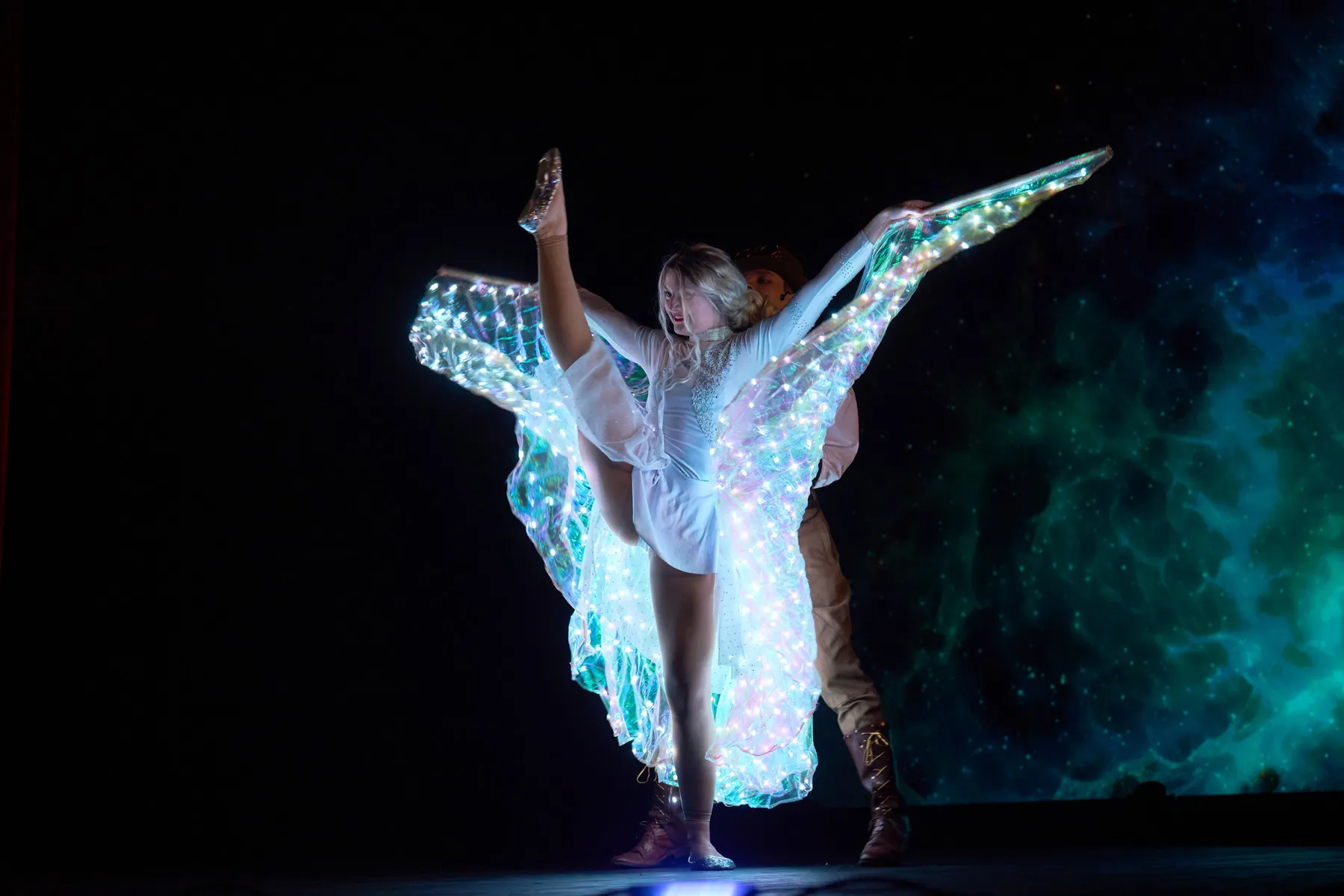An acrobatic duo in glowing LED costumes holding a lift figure
