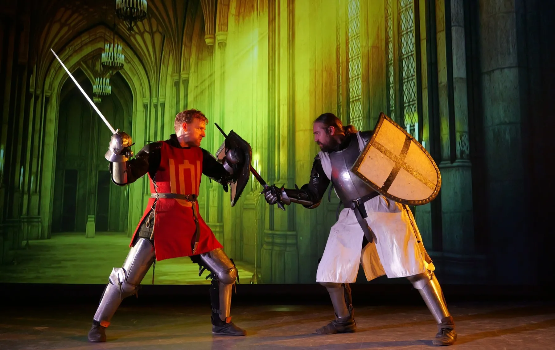 Two knights duel on stage in front of a projected gothic hall