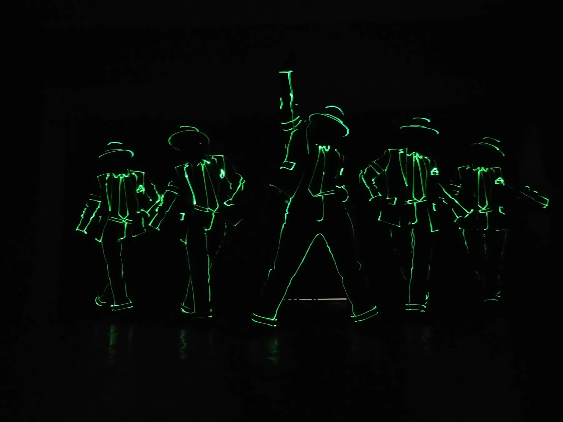 A group of dancers in light-outline costumes on a darkened stage