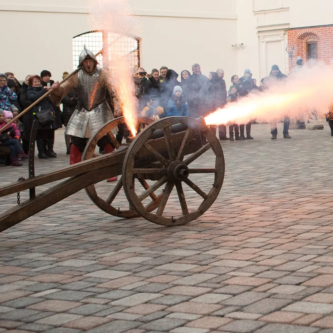 An armored performer fires the cannon with a bright flame in daylight