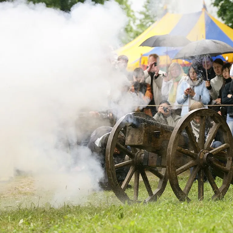 A cannon fires a burst of smoke beside a colourful circus tent