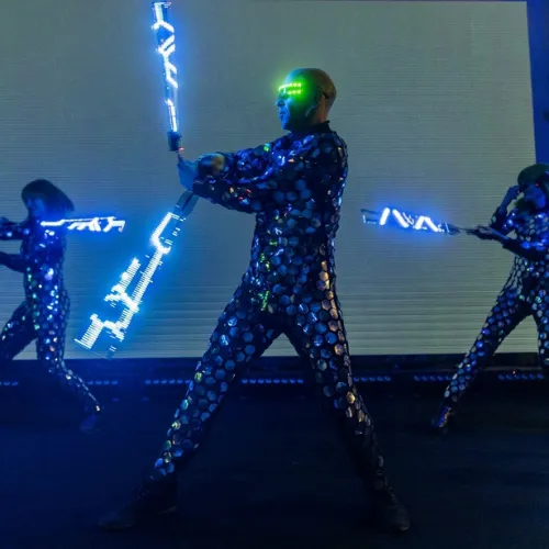 Three performers pose on stage holding glowing LED staffs