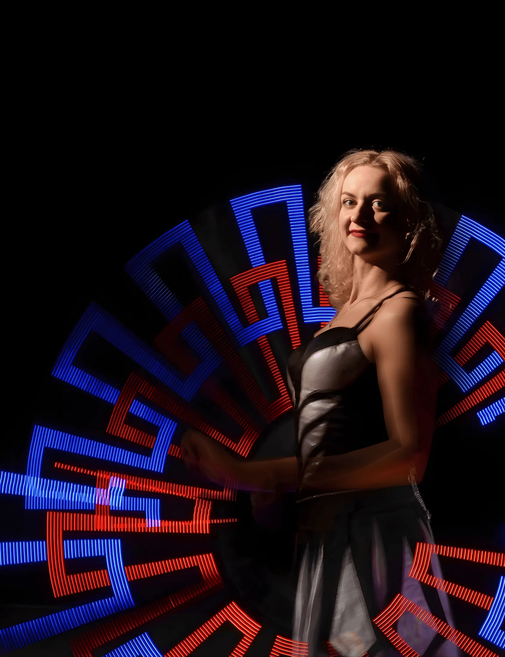 A performer paints a blue and red radiating pattern in the air with an LED hoop
