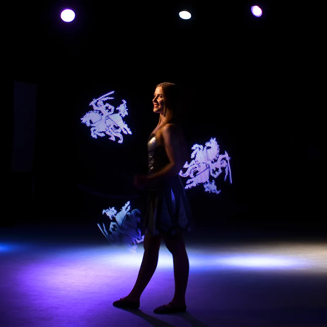 A performer on stage surrounded by glowing wing-shaped light patterns