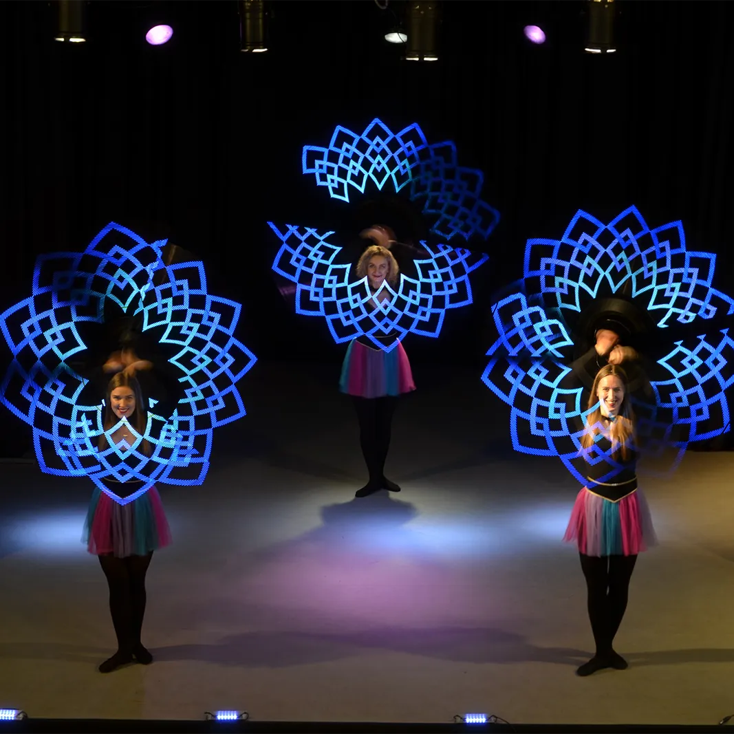 Three performers synchronise LED hoops to paint glowing mandala patterns