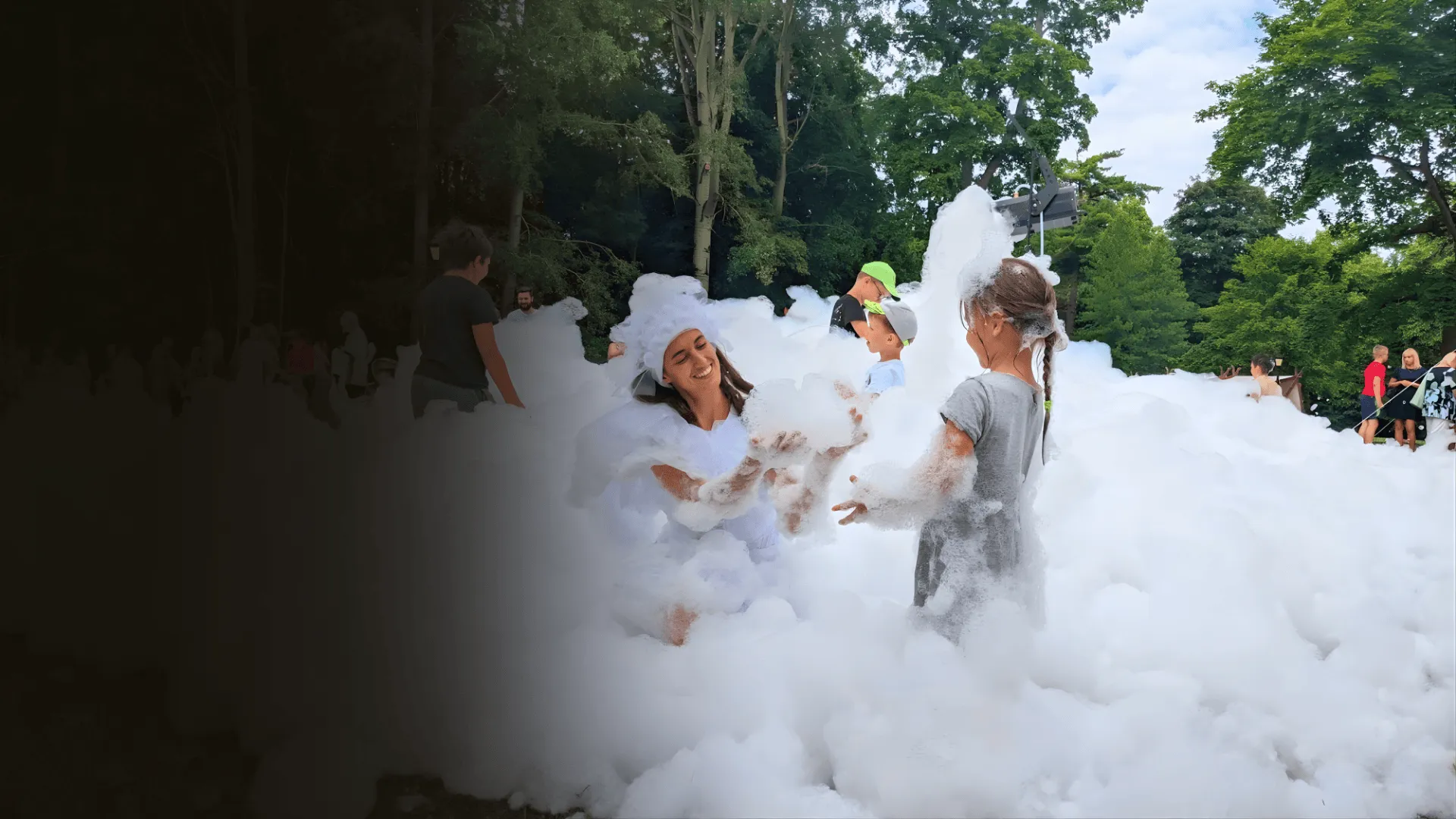 A white foam-fairy character plays with children in a cloud of foam