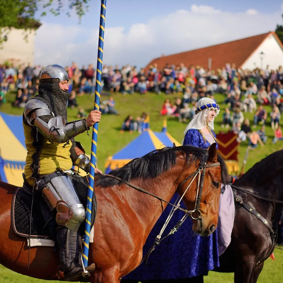 A rider with a long lance and a lady in a blue gown in the arena among spectators