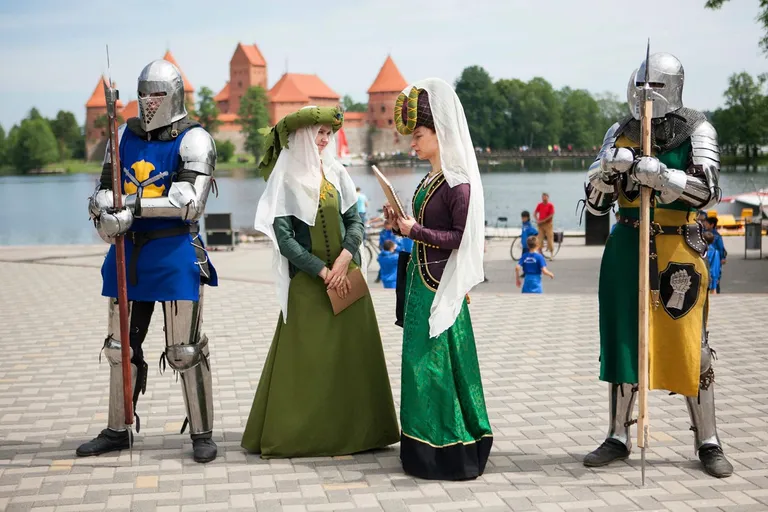 Bruņinieki un dāmas vēsturiskos tērpos pie Traķu pils ezera krastmalas
