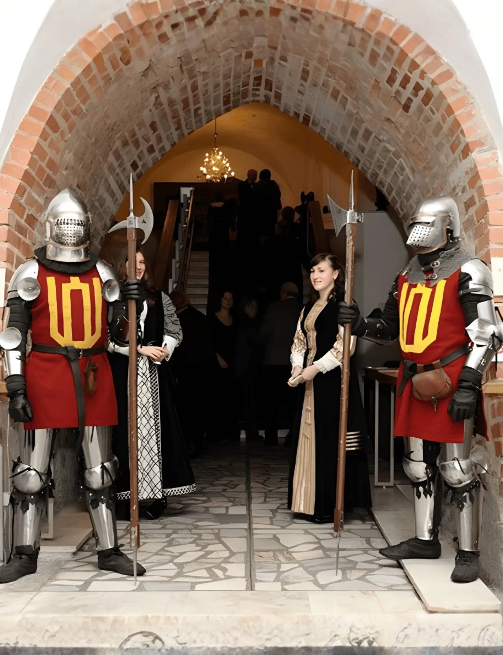 Knights on guard beside a vaulted entrance arch as guests pass through