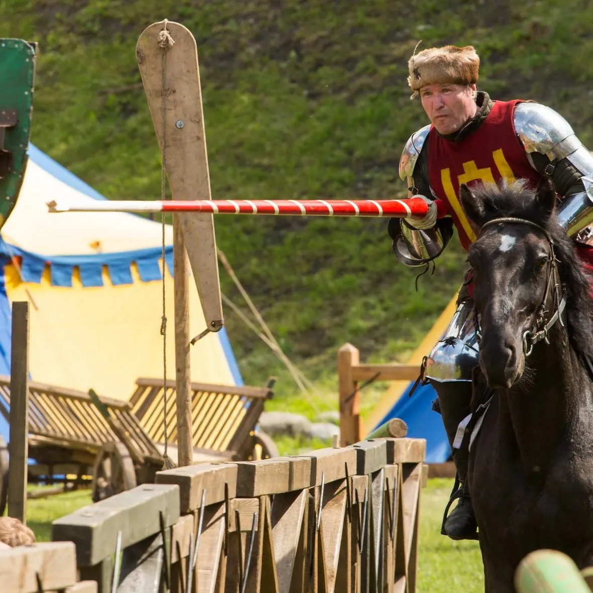 A mounted knight charges a ring target with a lance in the tournament arena