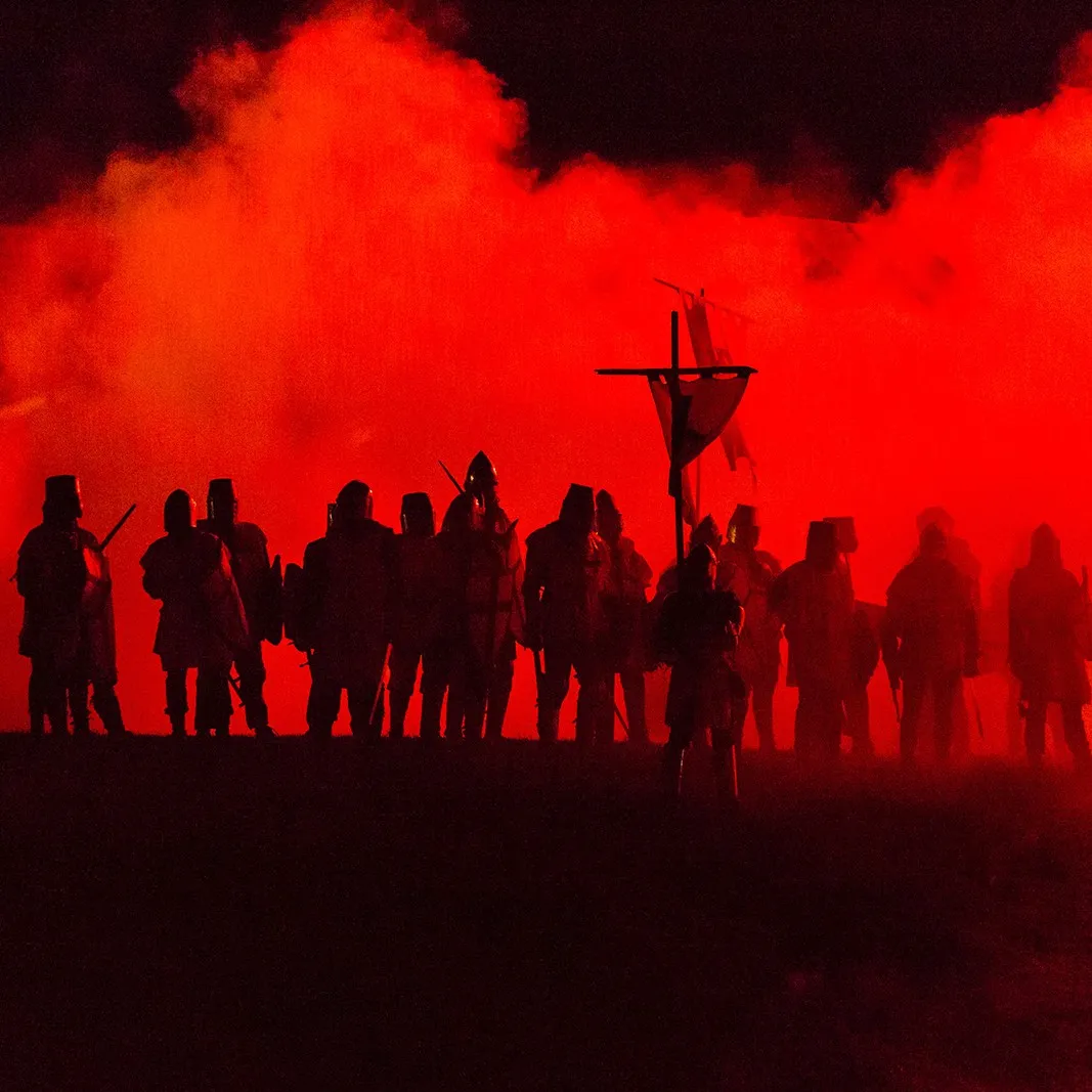 Silhouettes of a knight troop against red stage smoke