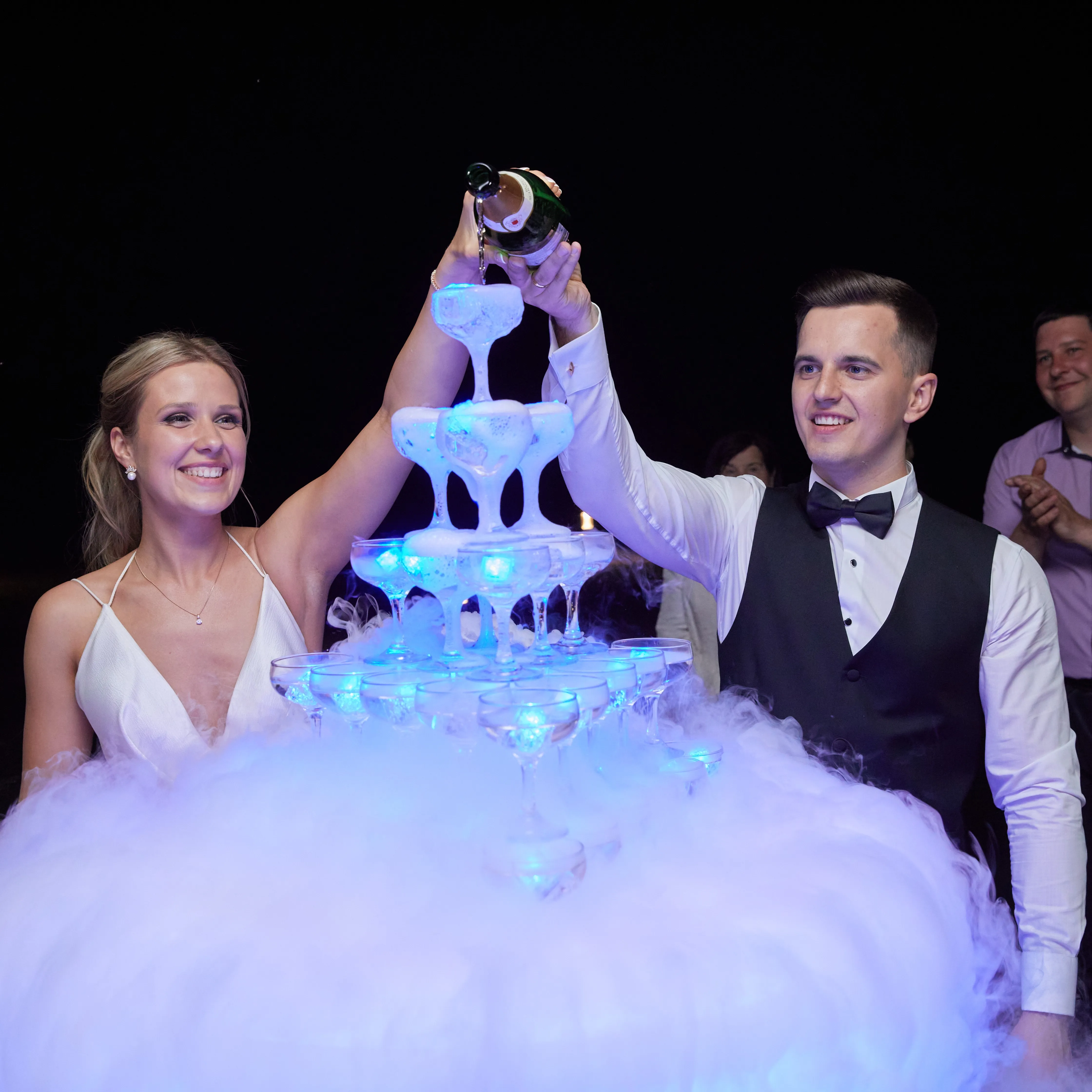 A couple pours champagne into a glass tower lit with cold spark effects