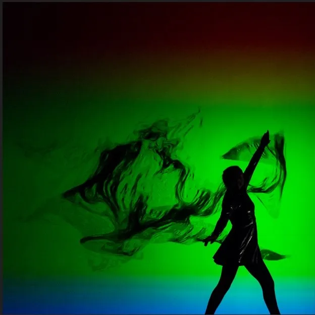 A dancer in motion against a green smoke-swirl projection