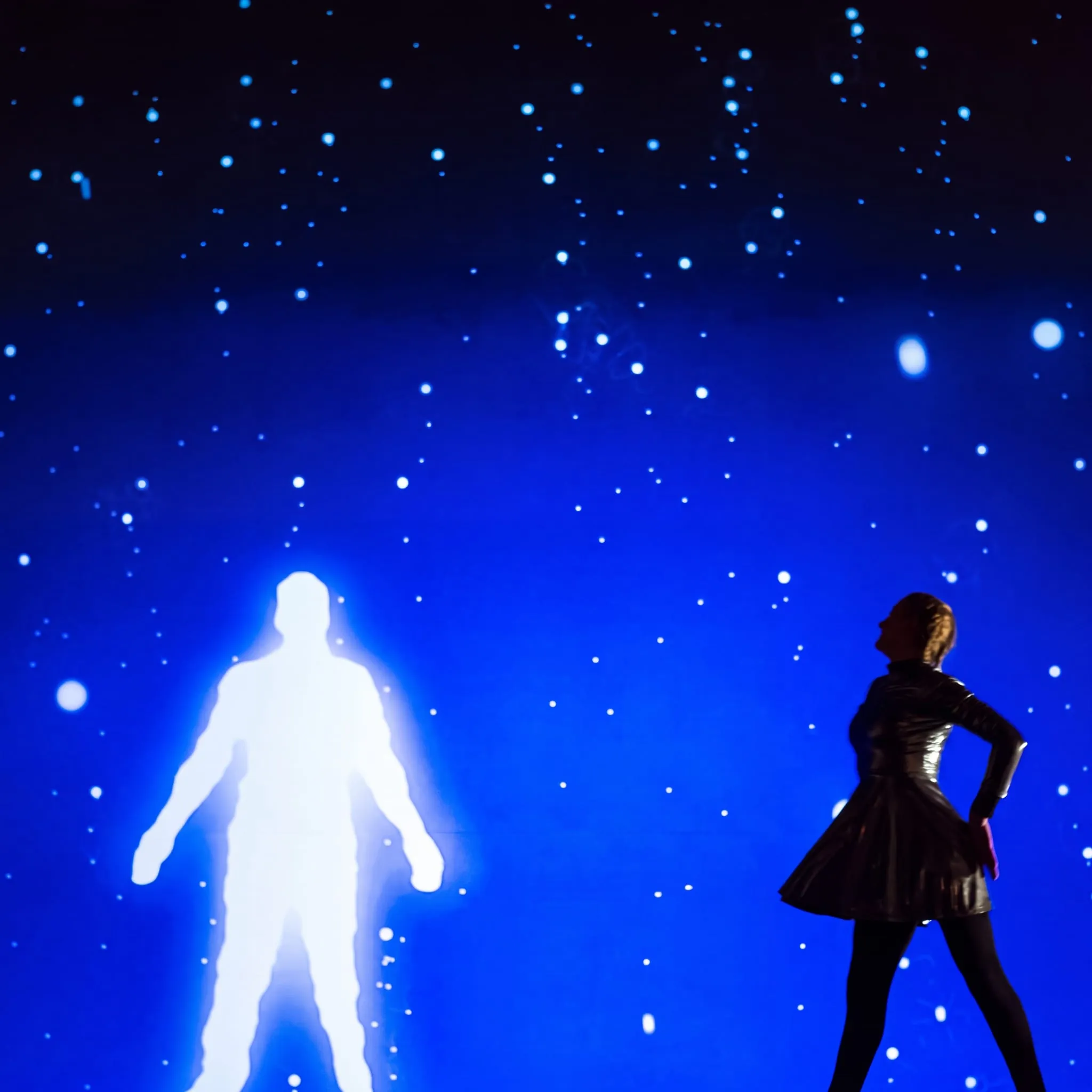 A performer stands beside a glowing human-figure projection