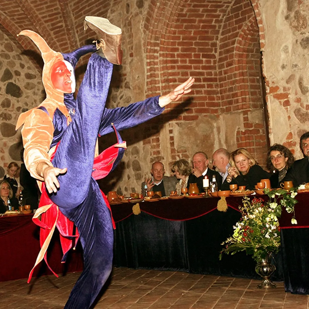 A jester leaps beside the royal feast table with guests