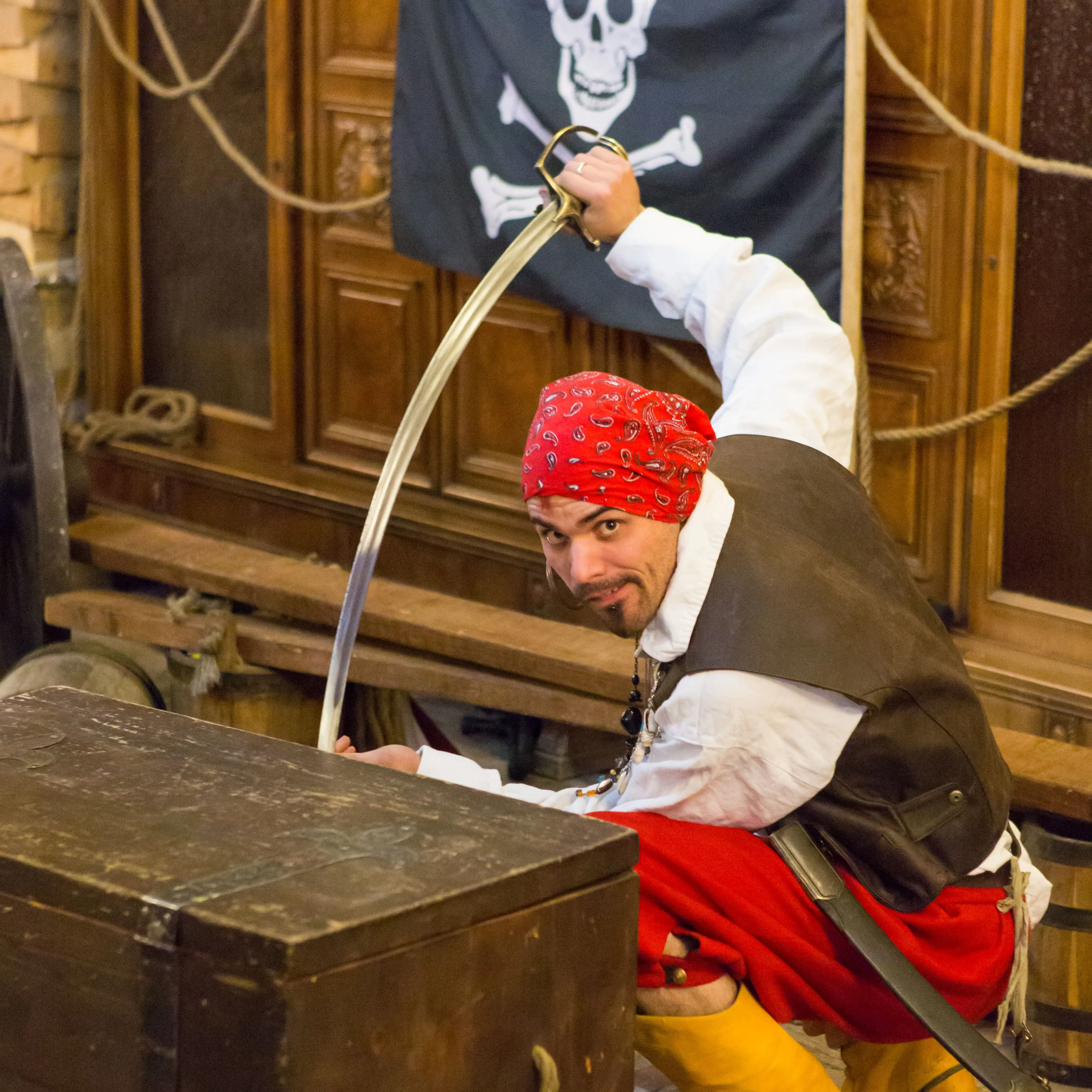 A pirate with a sword leaning over a treasure chest