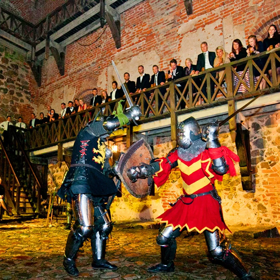 A knights' duel in the feast hall, watched by guests from the balcony