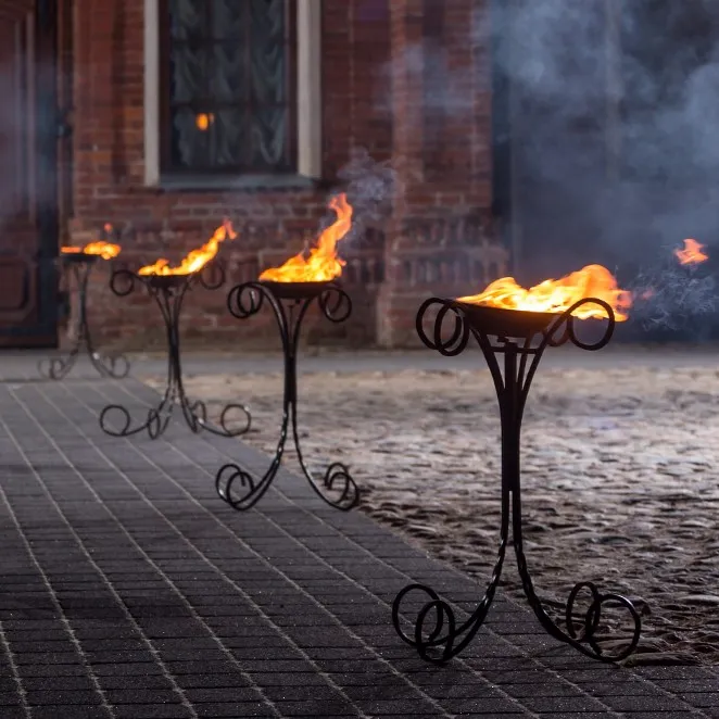 Fire stands glowing through mist along a path by a historic building