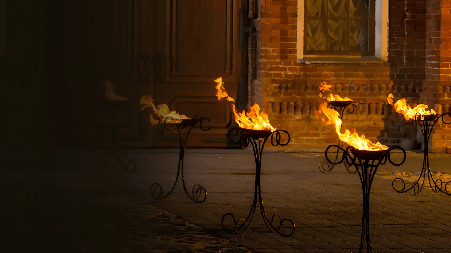 A row of lit fire stands along a brick-wall path at night