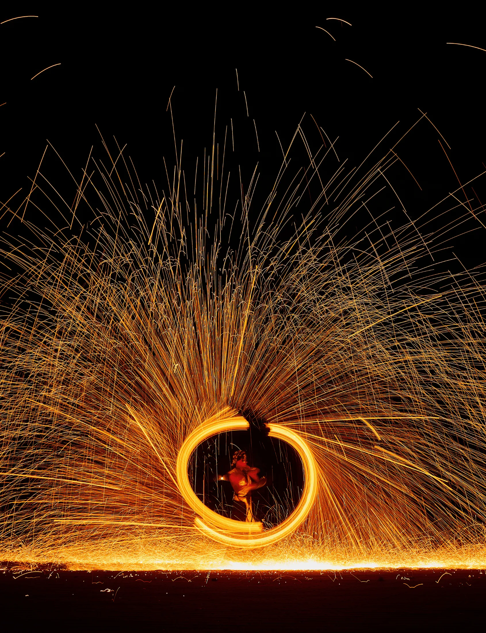 A performer spins inside a ring of fire as a shower of sparks flies outward