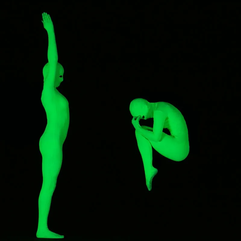 Two glowing performers sit facing each other with their feet touching