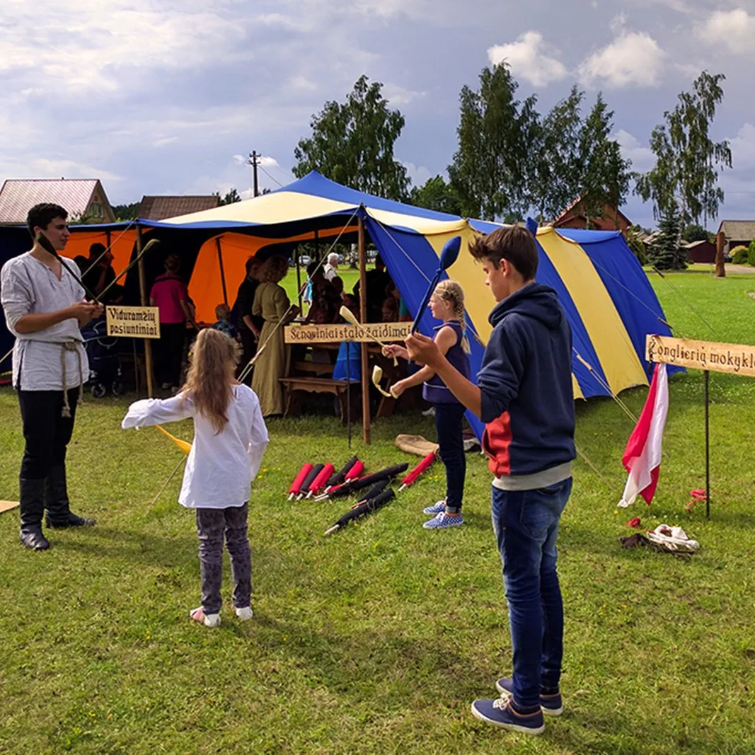 An instructor teaches children to juggle beside a striped tent with a signboard
