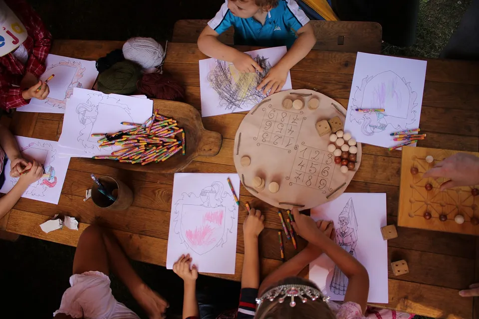 Children drawing their own coats of arms at a wooden table with pencils