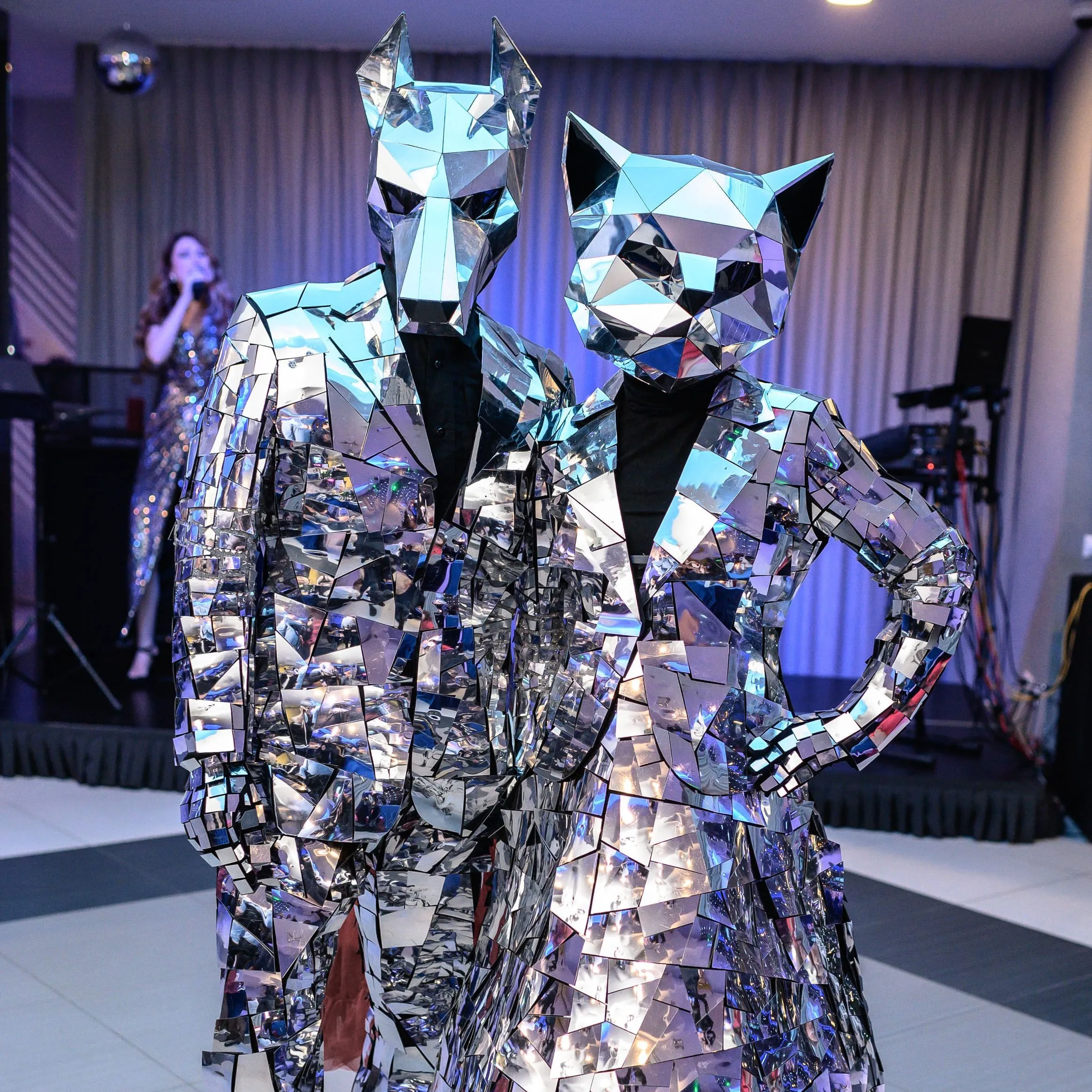 Mirror-mosaic wolf and cat-head characters in an event hall with a singer in the background