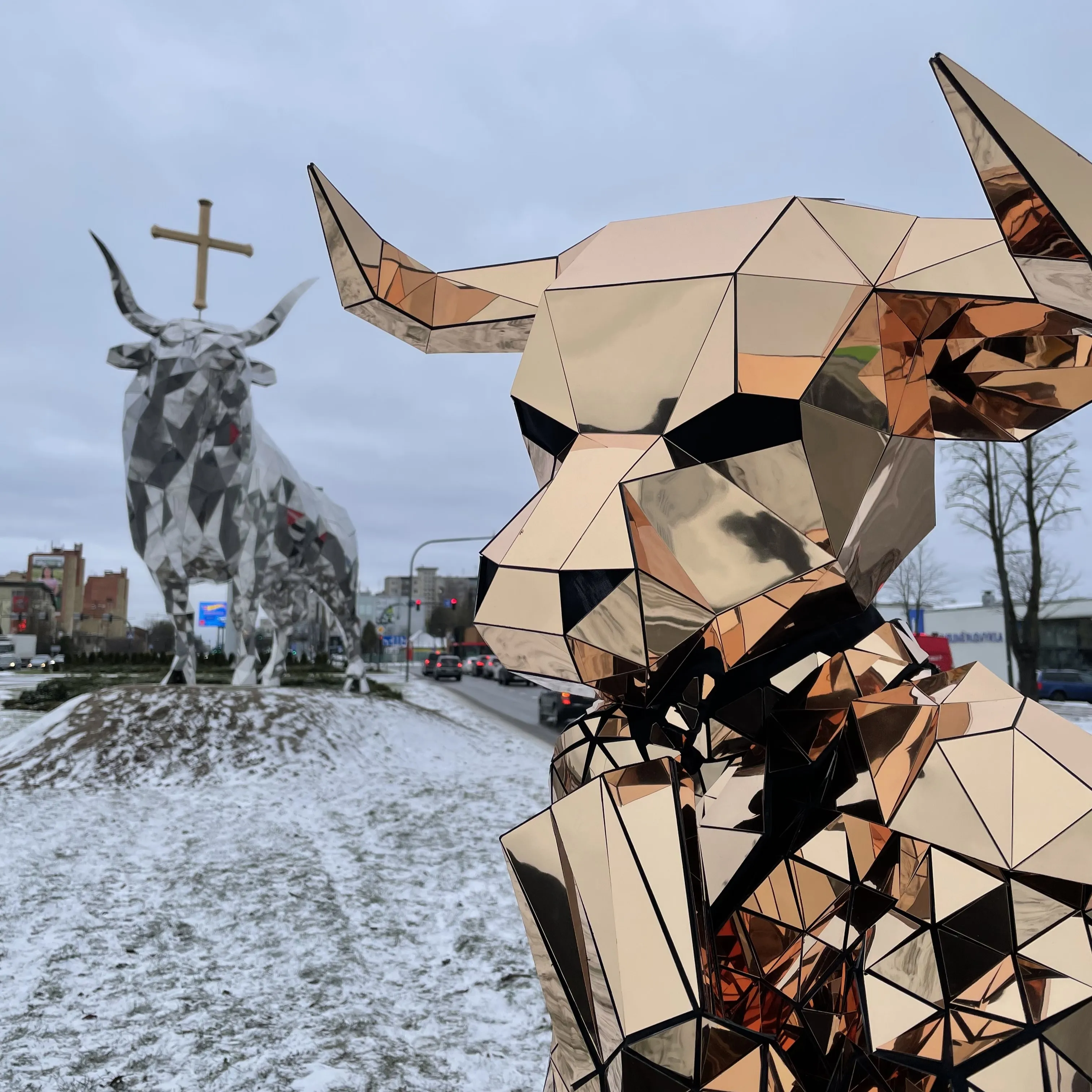 Mirror-mosaic bull character posing beside a metal bull statue in the city