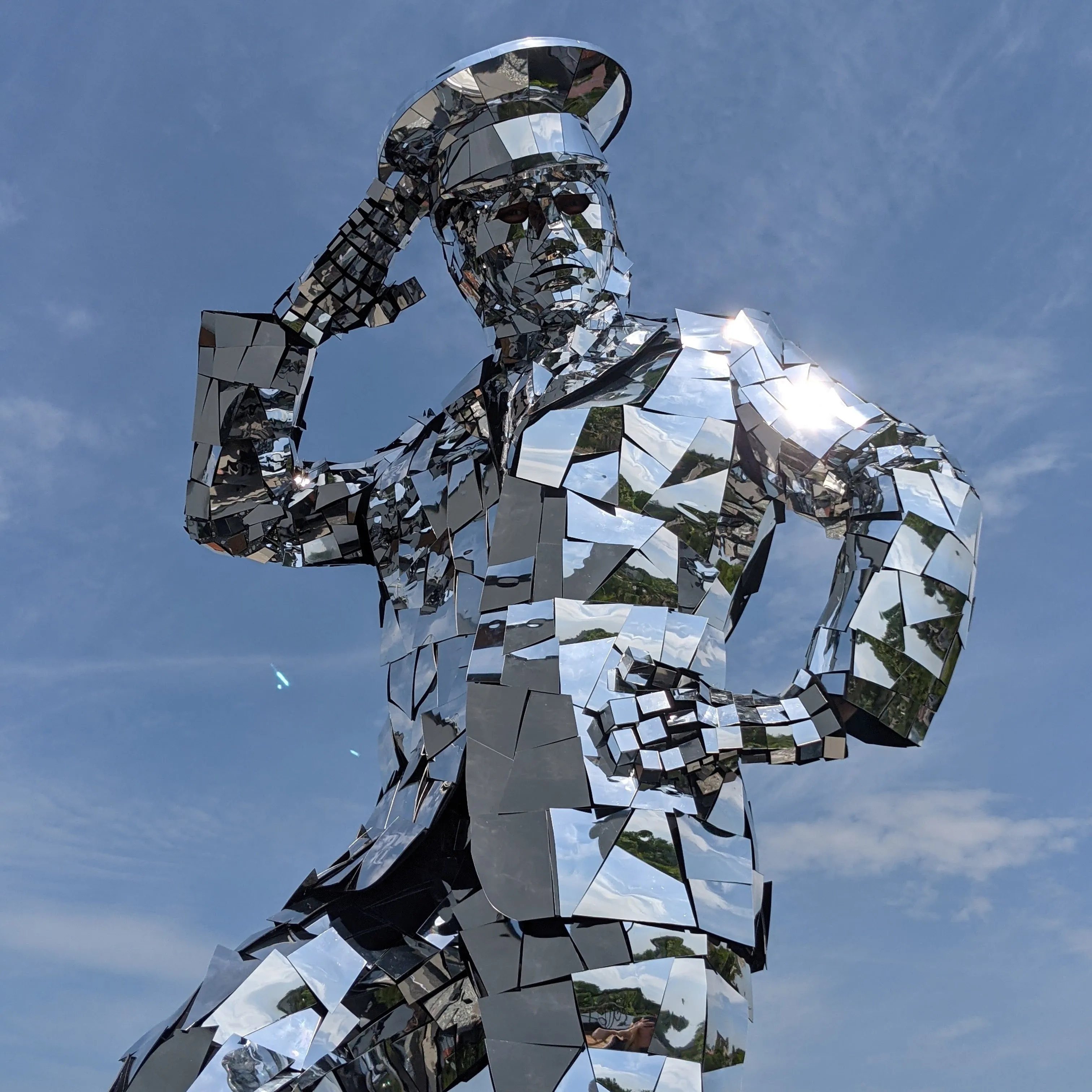 Mirror-mosaic character wearing a cap, seen from below against a blue sky