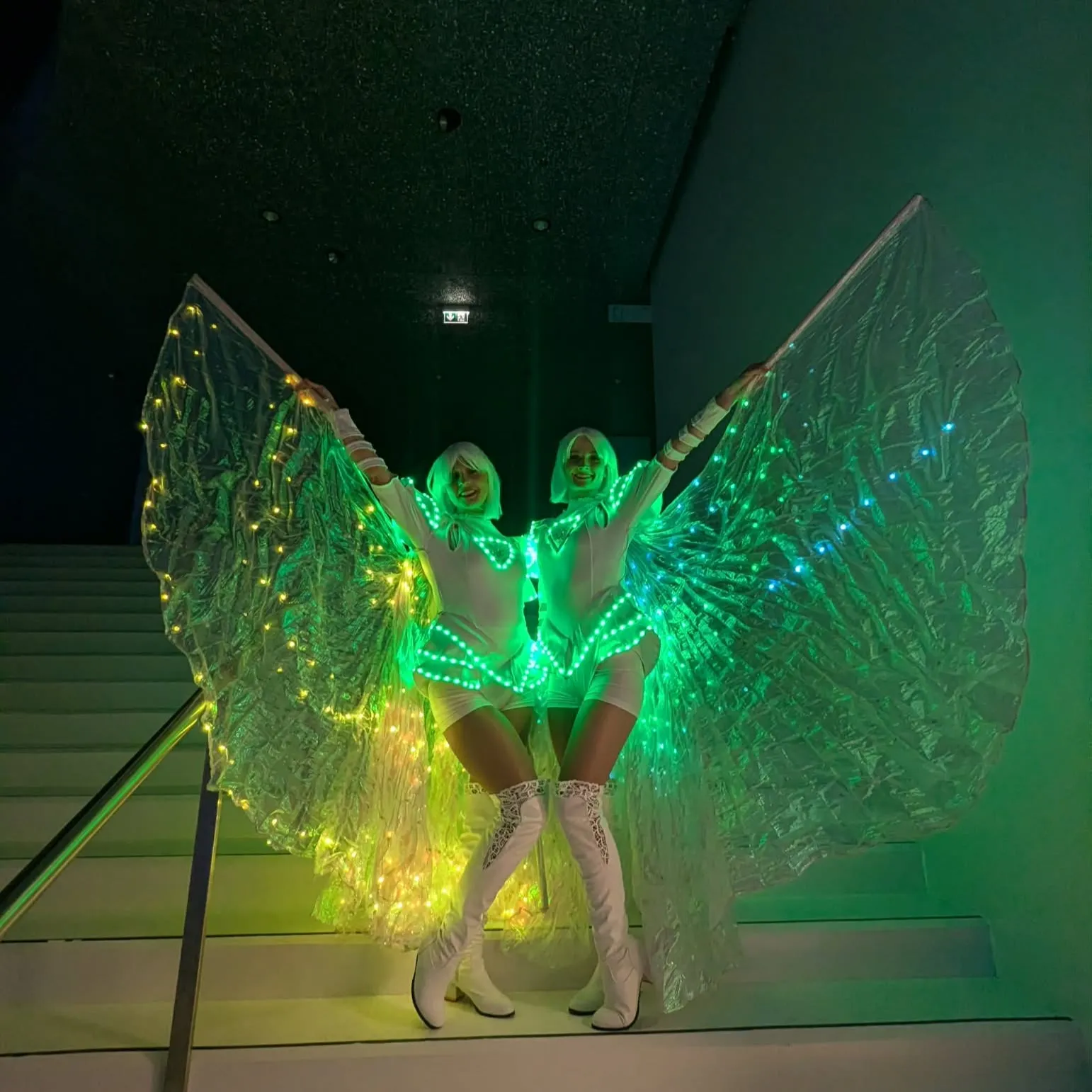 Two dancers with glowing green LED wings on a staircase