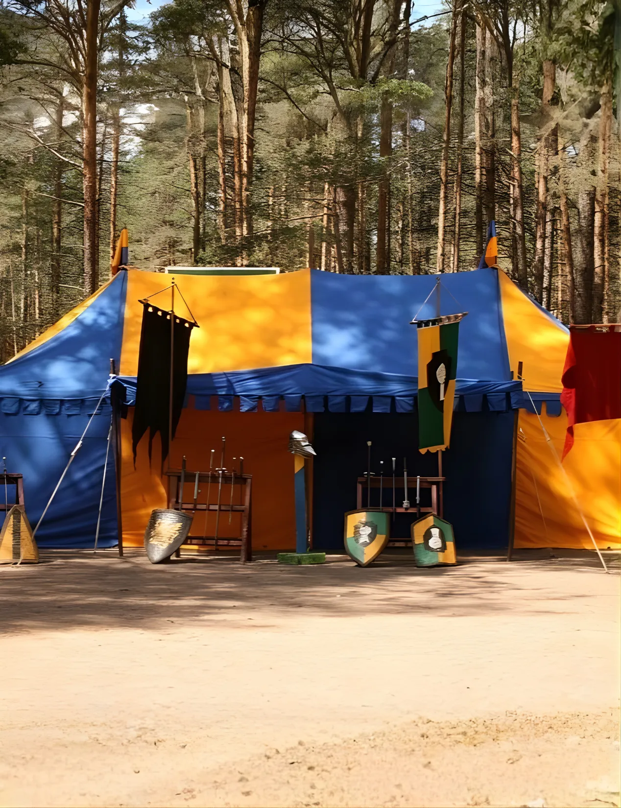 A two-tone blue and yellow medieval tent with a weapon rack by the forest