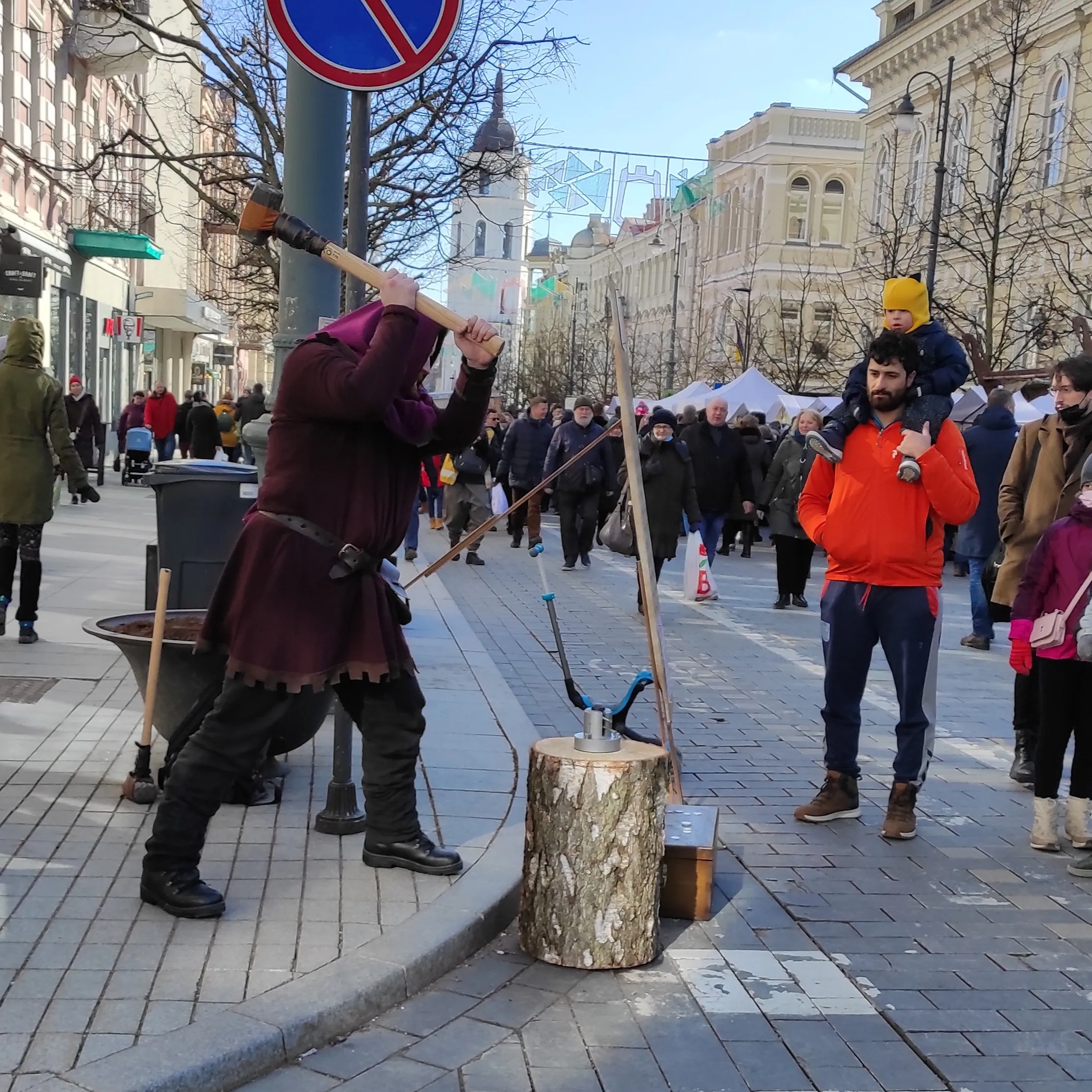 A man in medieval costume strikes a coin on a city street in front of onlookers