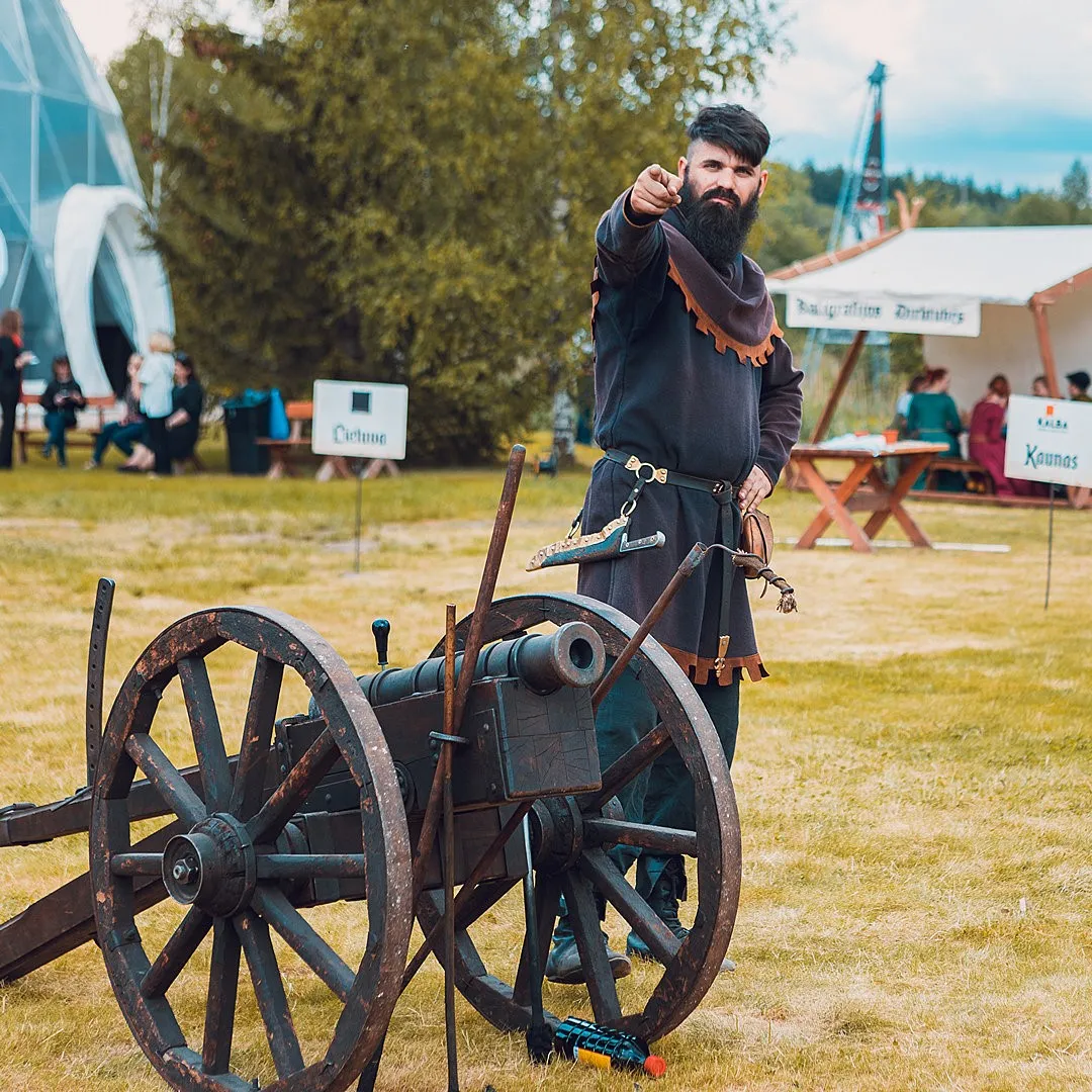 A man in medieval costume gestures to the crowd beside a cannon