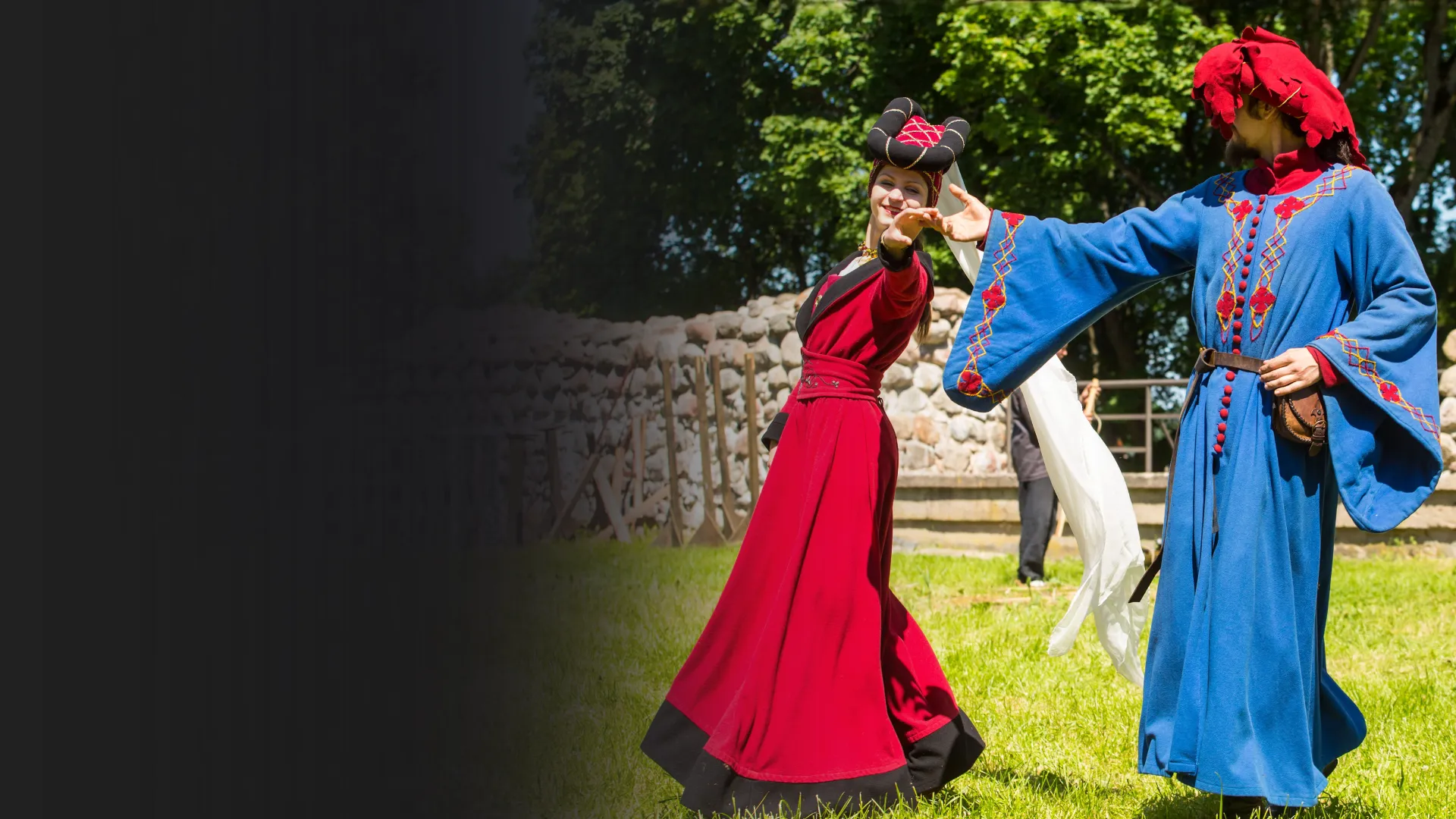 A couple in red and blue medieval costume dances on the grass