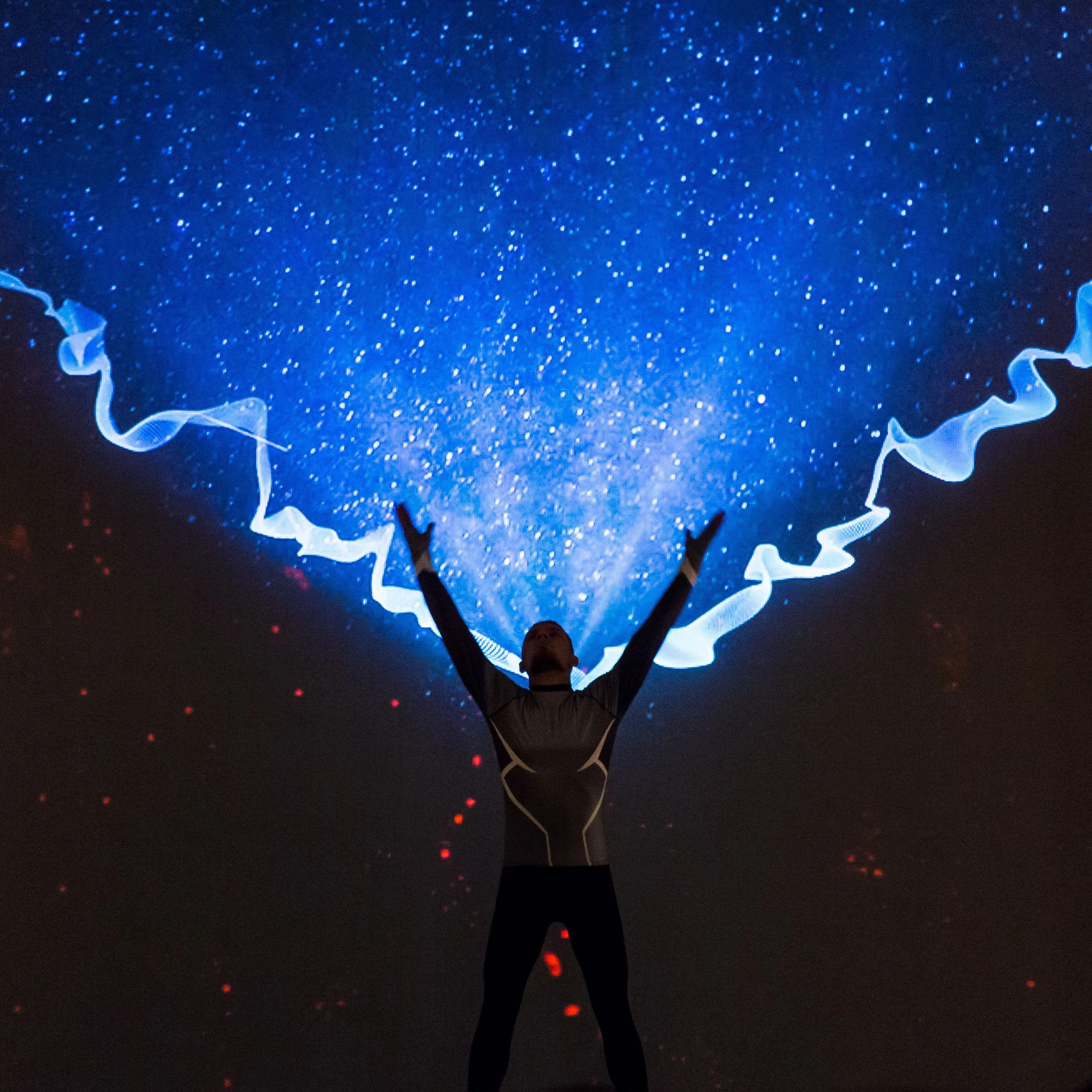 A performer raises both arms into a blue wave projection on stage