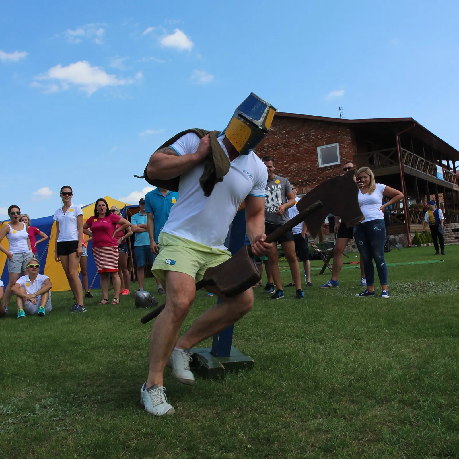 A man in a knight's helmet strikes a padded weapon against a post target