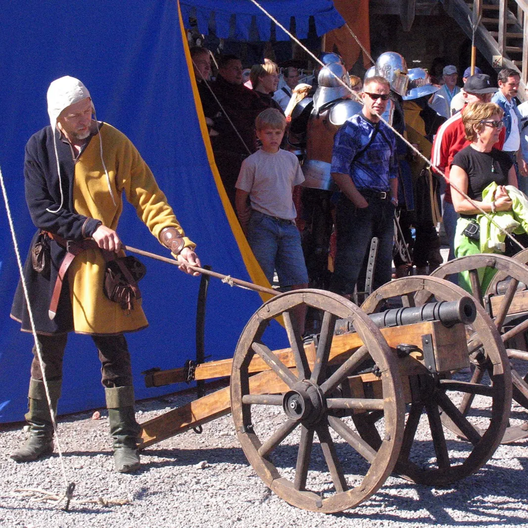 A man in a yellow tunic pulls a cannon by rope past the crowd