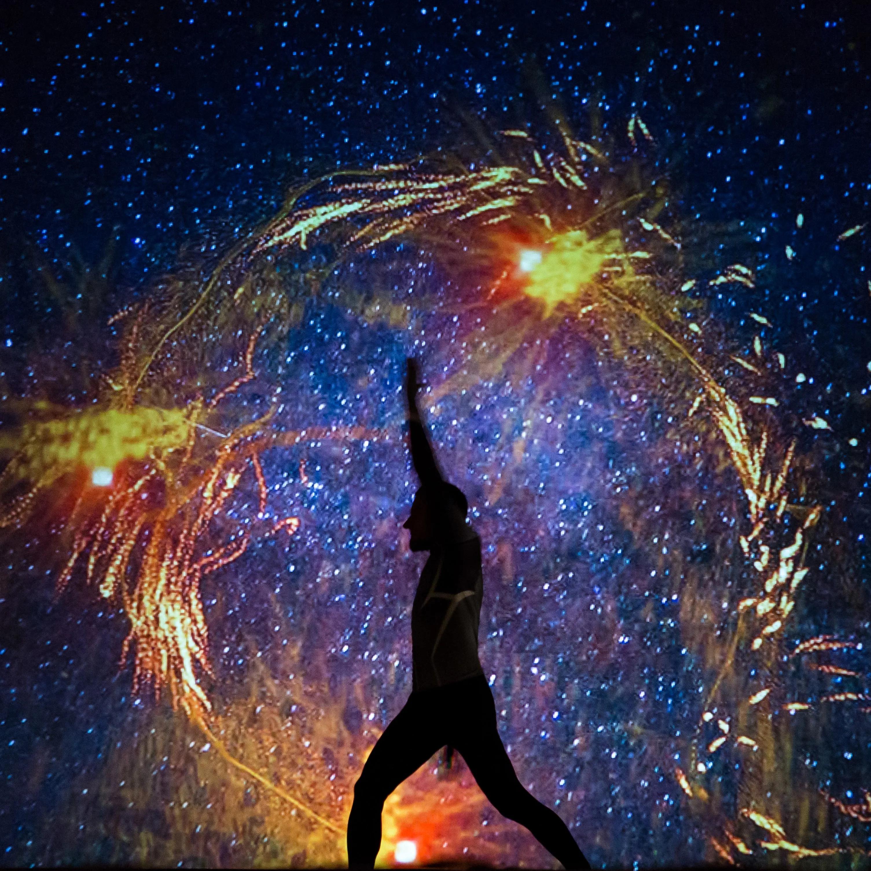 A man strikes a dance pose against a fiery orange projection